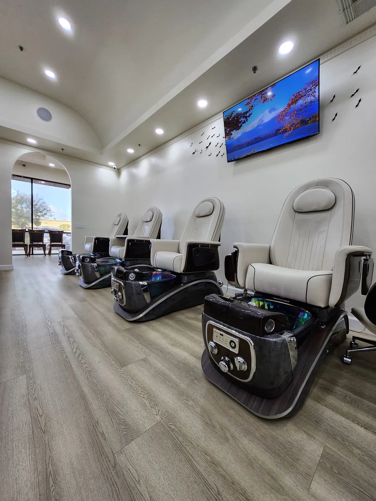 Pedicure chairs beneath a wall-mounted TV, with an arched window beyond
